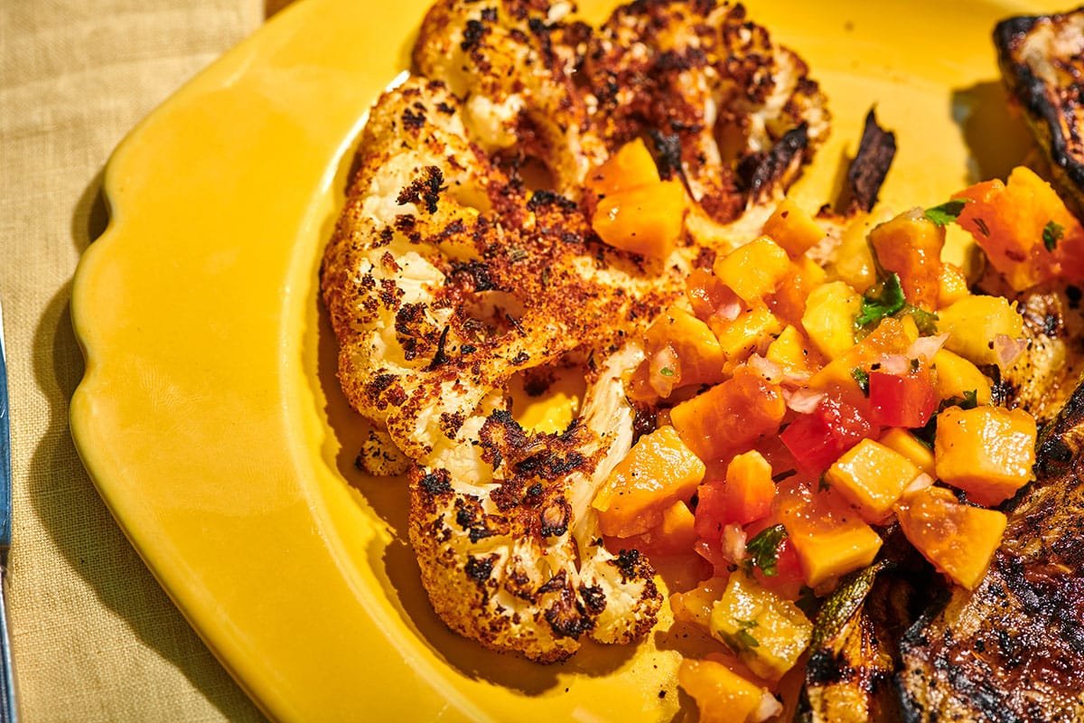 Grilled blackened cauliflower steak on yellow plate with salsa.