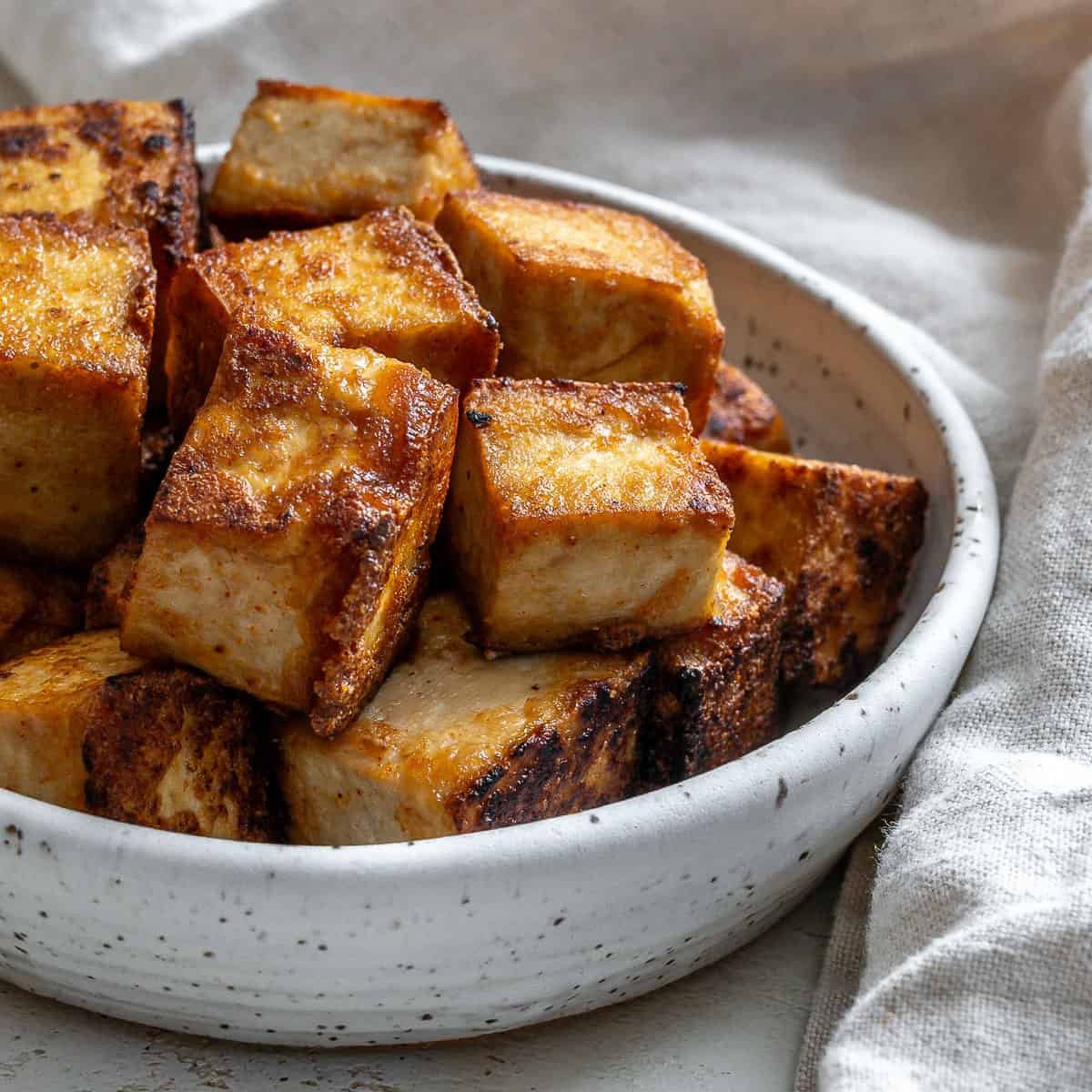 Fried tofu in a white speckled bowl with a light grey napkin beside it.